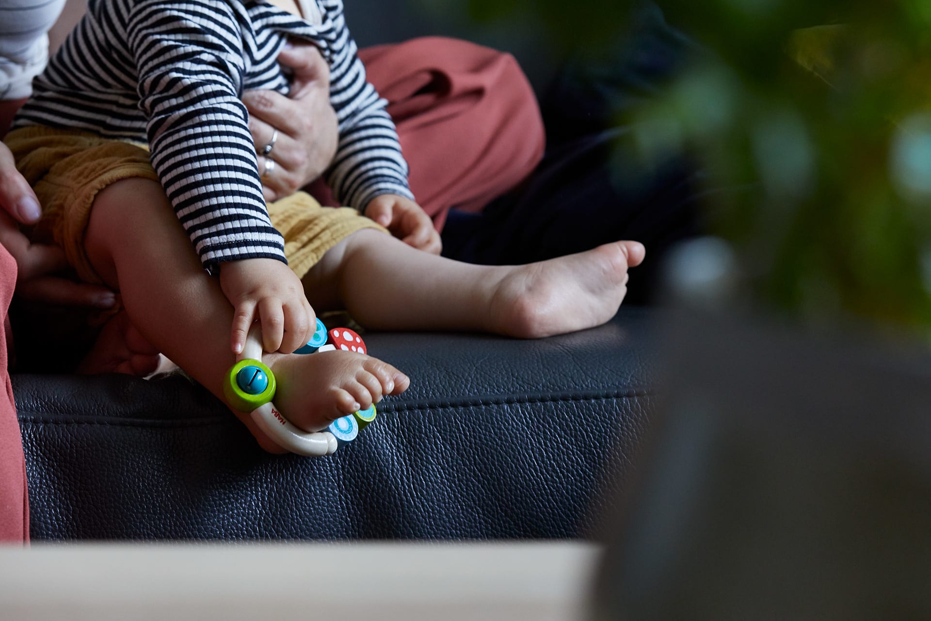  Spielerisch lernen |  Baby sitzt auf Mamas Schoß, hat Greifling um den Fuß gelegt