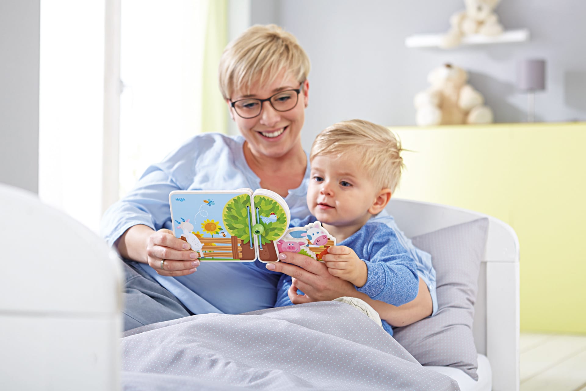 Spielerische Sprachförderung von Kindern | Mutter sitzt mit Kleinkind zusammen im Bett und schauen sich ein Buch an