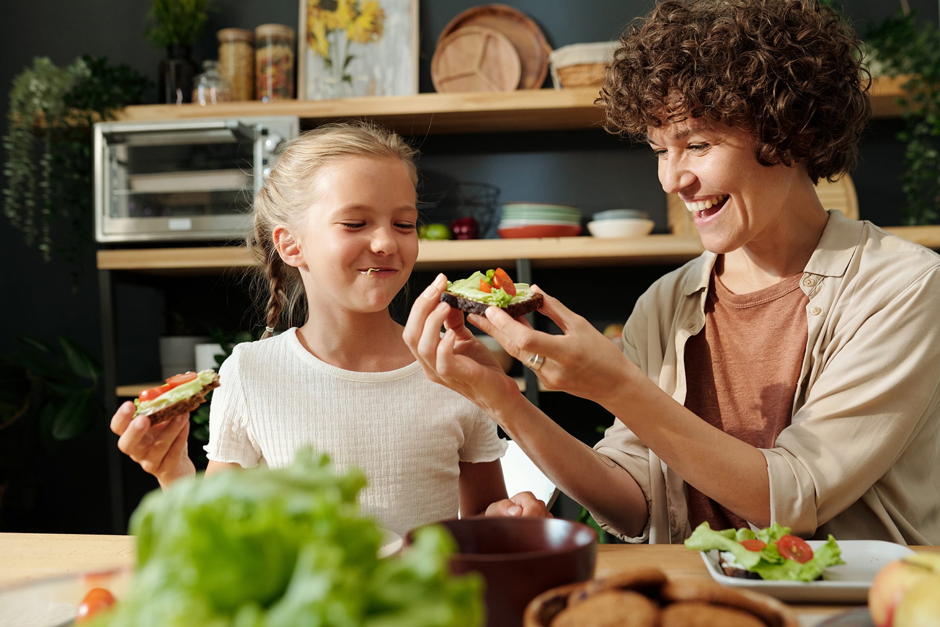 Kinder vegetarisch ernähren | Mutter und Tochter sitzen am Tisch und essen Tomaten- und Gurkenbrote