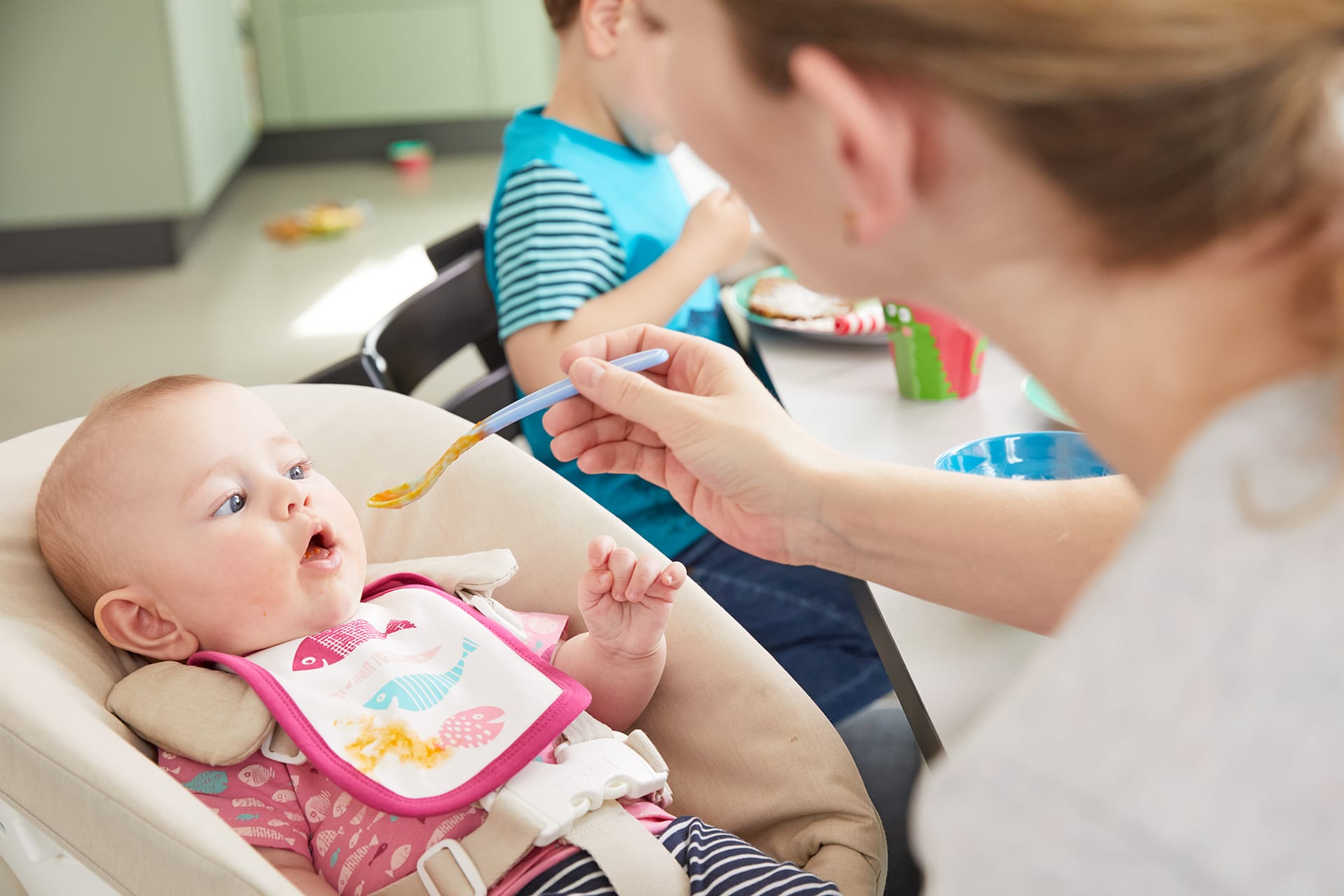 Verstopfung bei Babys | Mutter füttert Kind mit Brei. Baby liegt in einem Hochstuhl 