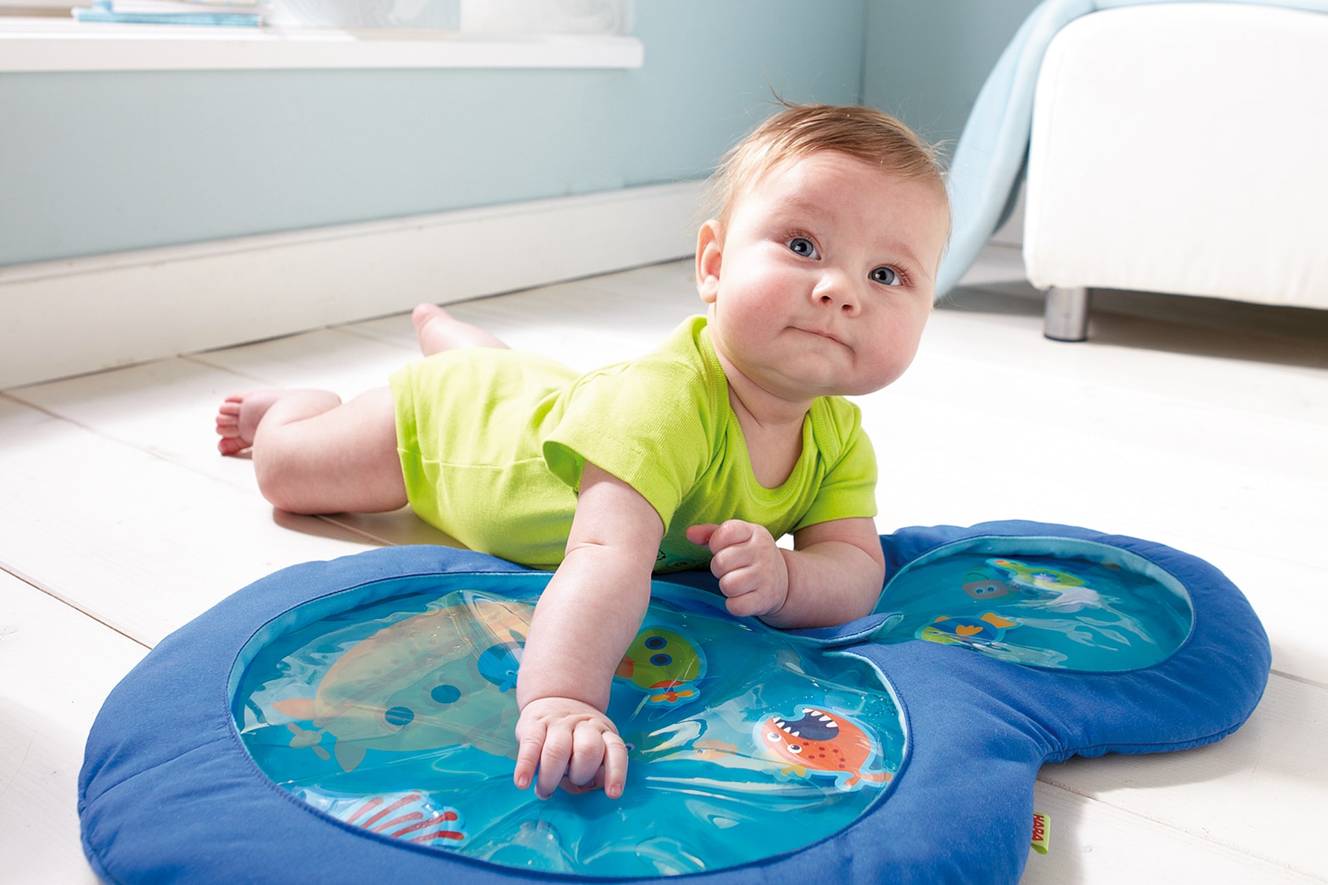 HABA Wasser-Spielmatten | Kleinkind mit grünen Kurzarmbody liegt auf dem Bauch auf einer blauen Wasserspielmatte