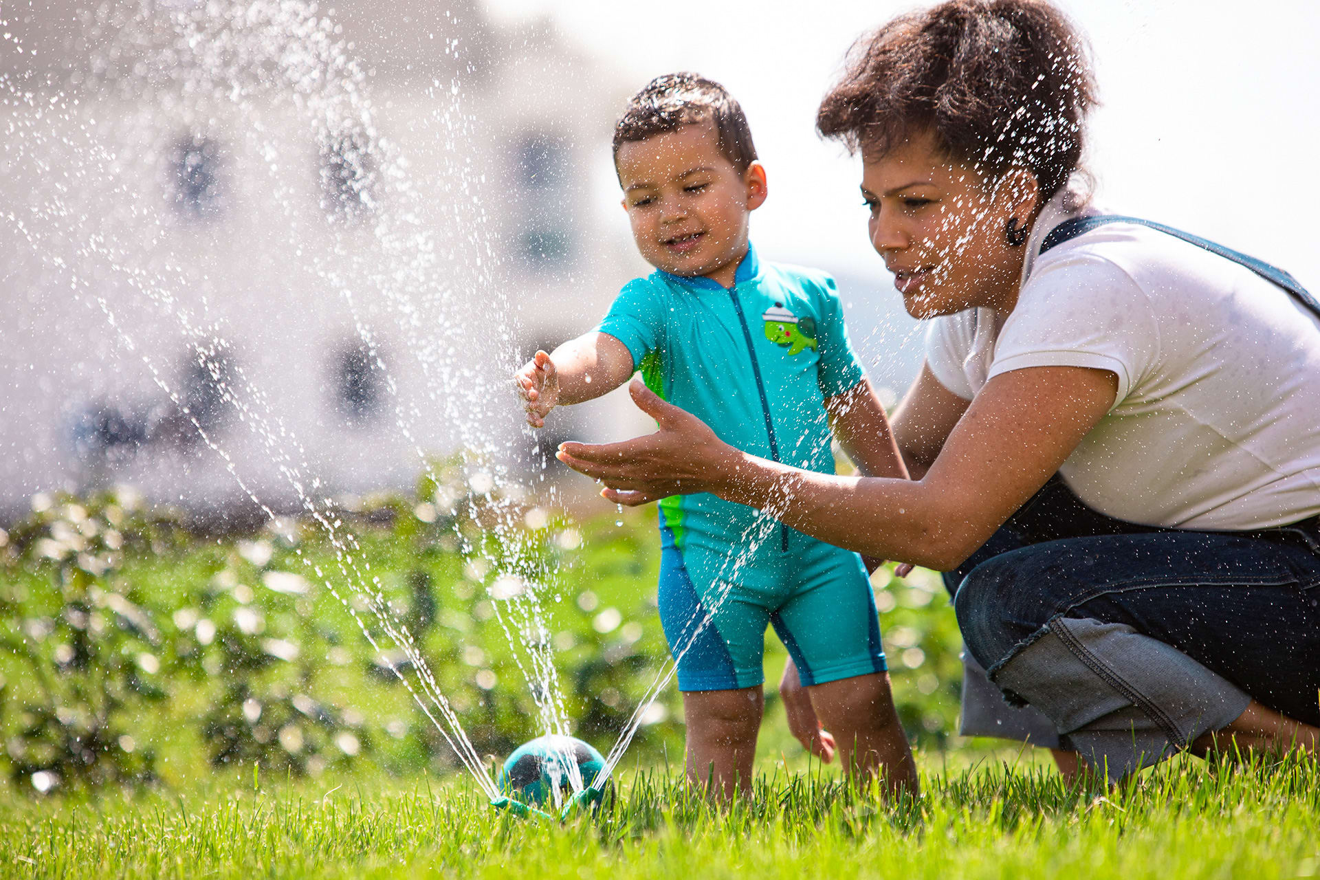 Wasserspiele draußen | Mutter spielt mit Kind an einer Wassersprinkler Anlage