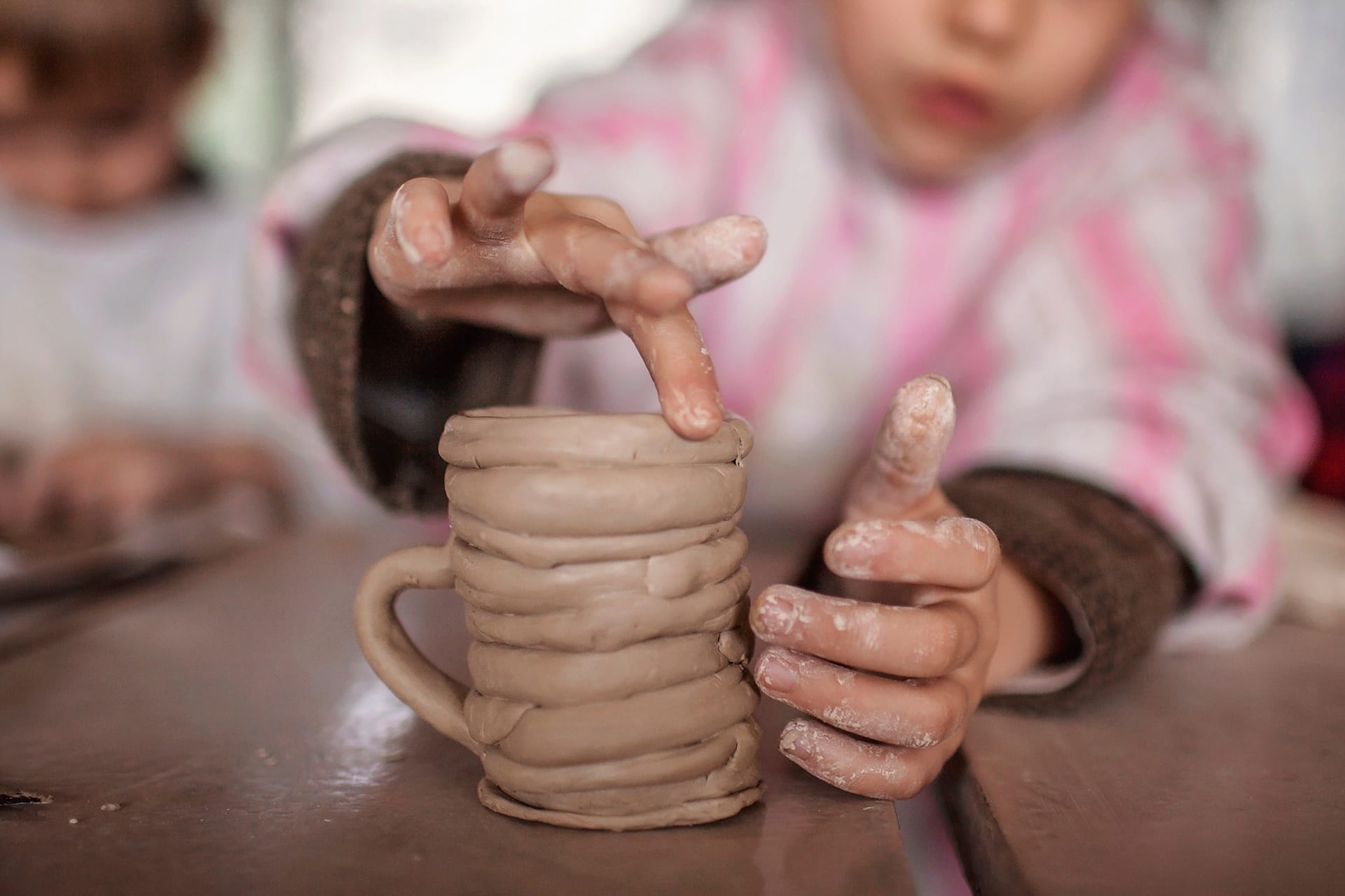 Modellieren mit Kindern | Kind sitzt am Tisch und modelliert mit den Fingern eine Tasse aus Ton