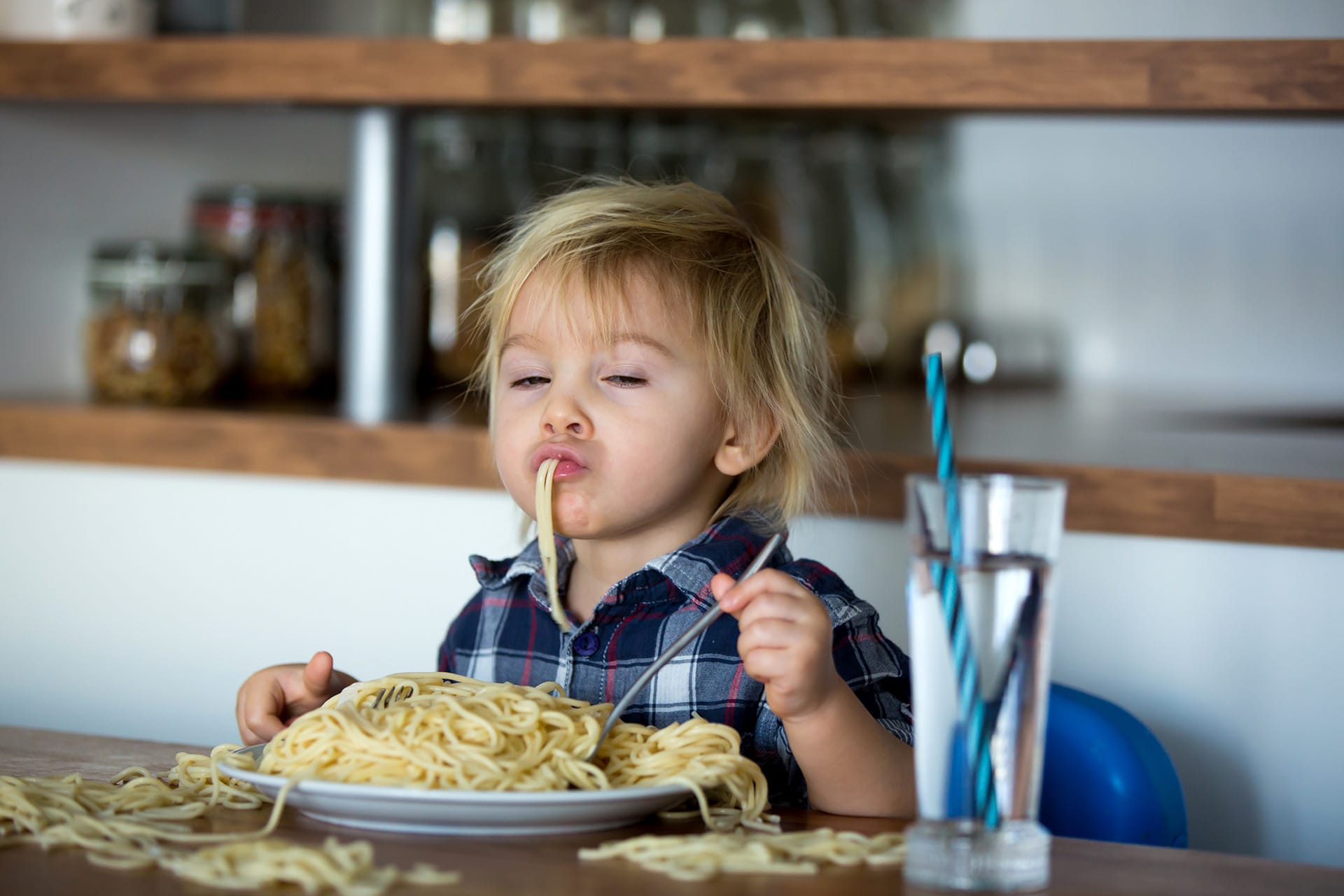 Kindern Tischmanieren beibringen | Kind isst Spaghetti vom Teller mit Finger und Gabel