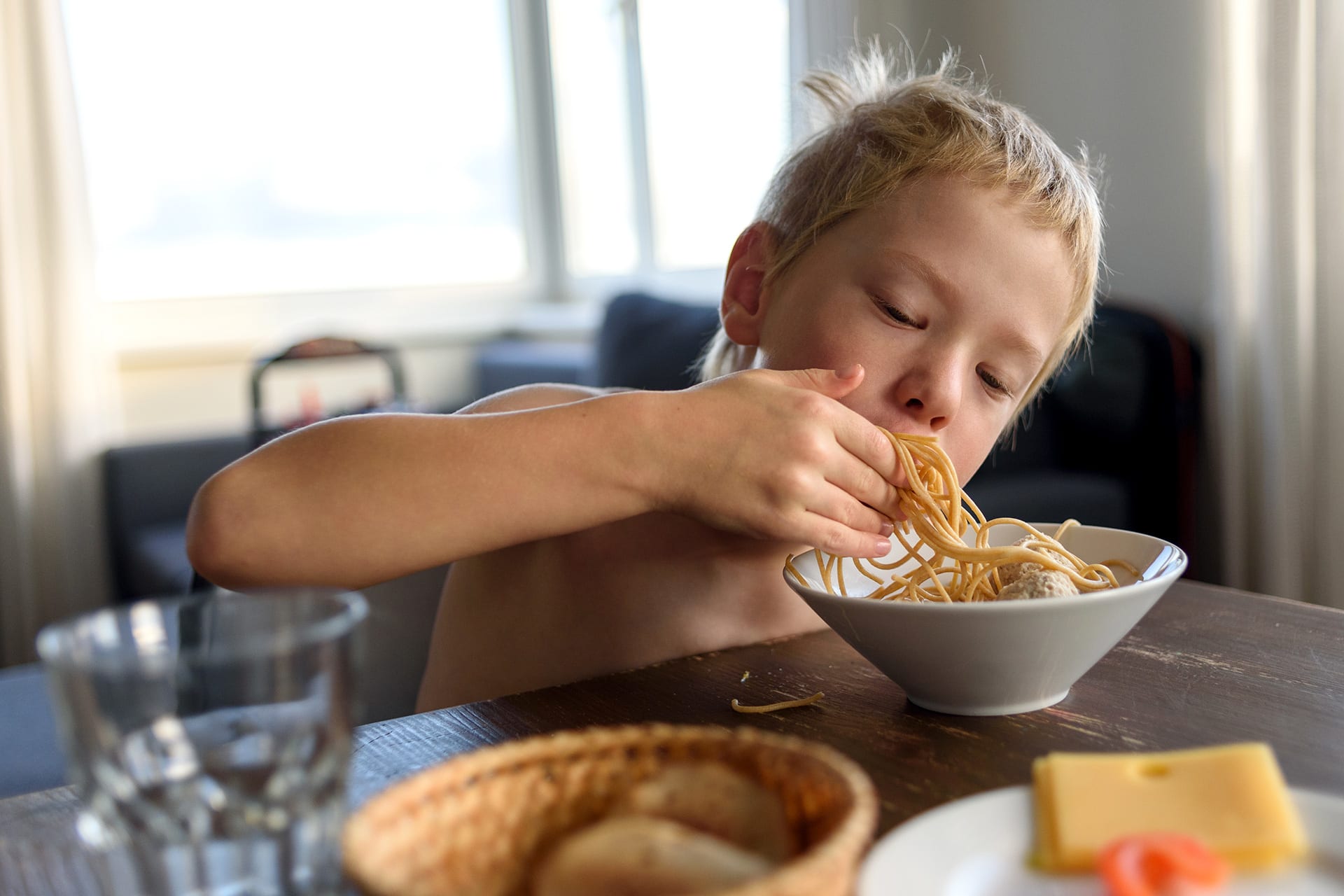 Kindern Tischmanieren beibringen | Junge isst Spaghetti mit Händen vom Teller
