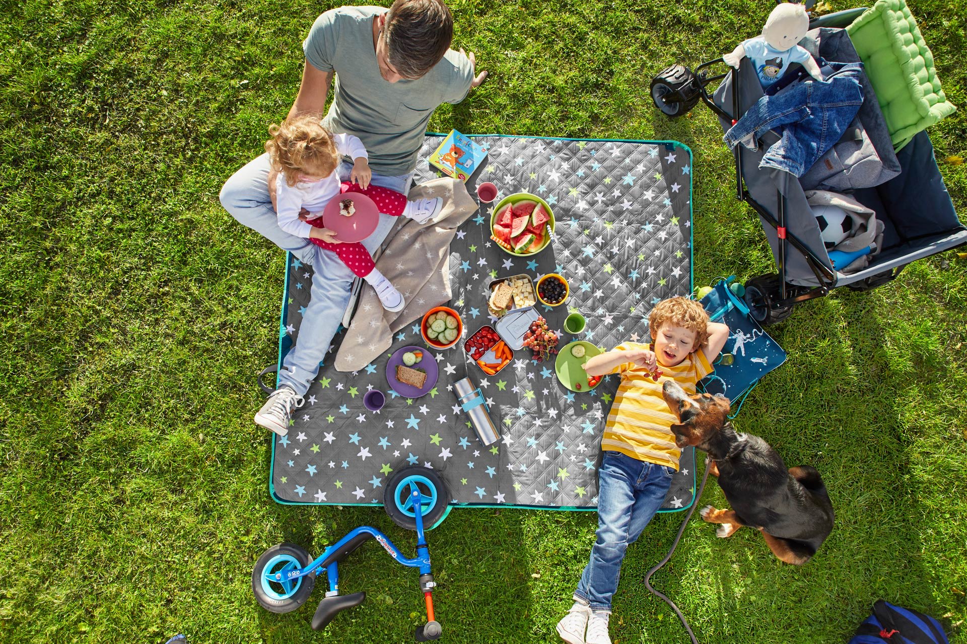 Wandern mit Kindern | Papa liegt mit seinen Töchtern auf einer Decke und macht Picknick