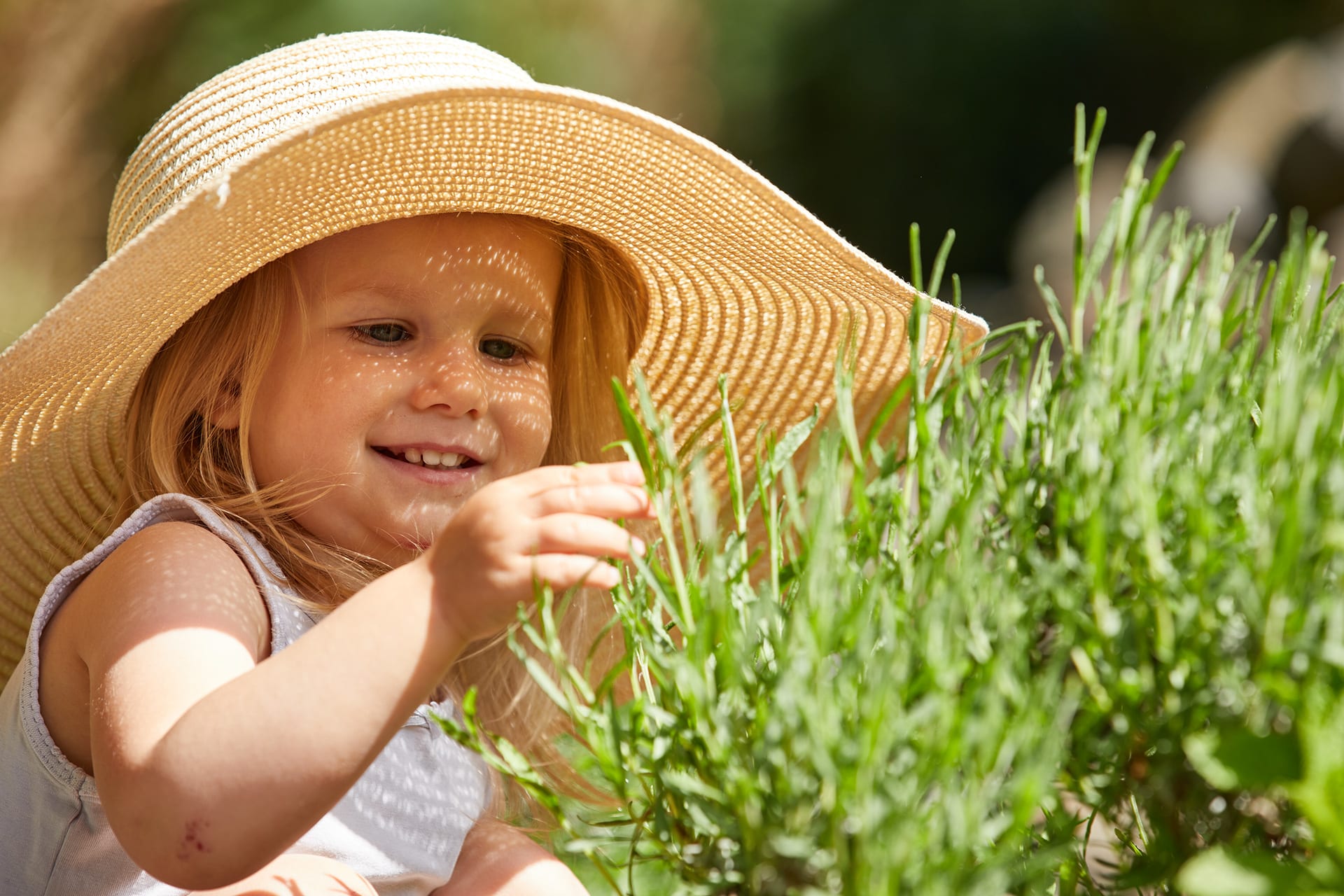 Basteln mit Kindern | Kind mit großem Sommerhut, sitzt vor Kräuterpflanzen