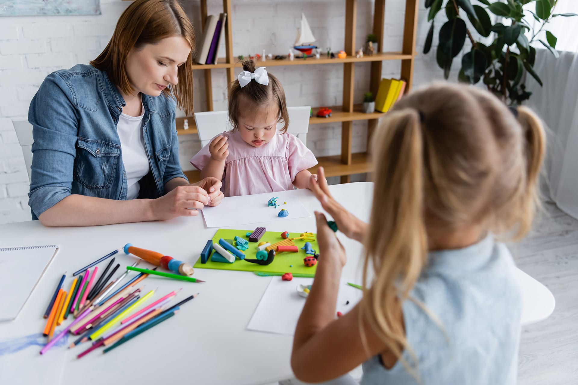 Integrativer Kindergarten | Erzieherin knetet und malt mit Kindern an einem Tisch