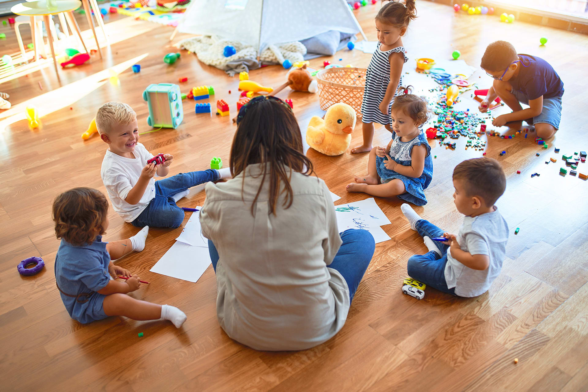 Integrativer Kindergarten | Kinder sitzen mit Erzieherin auf Boden