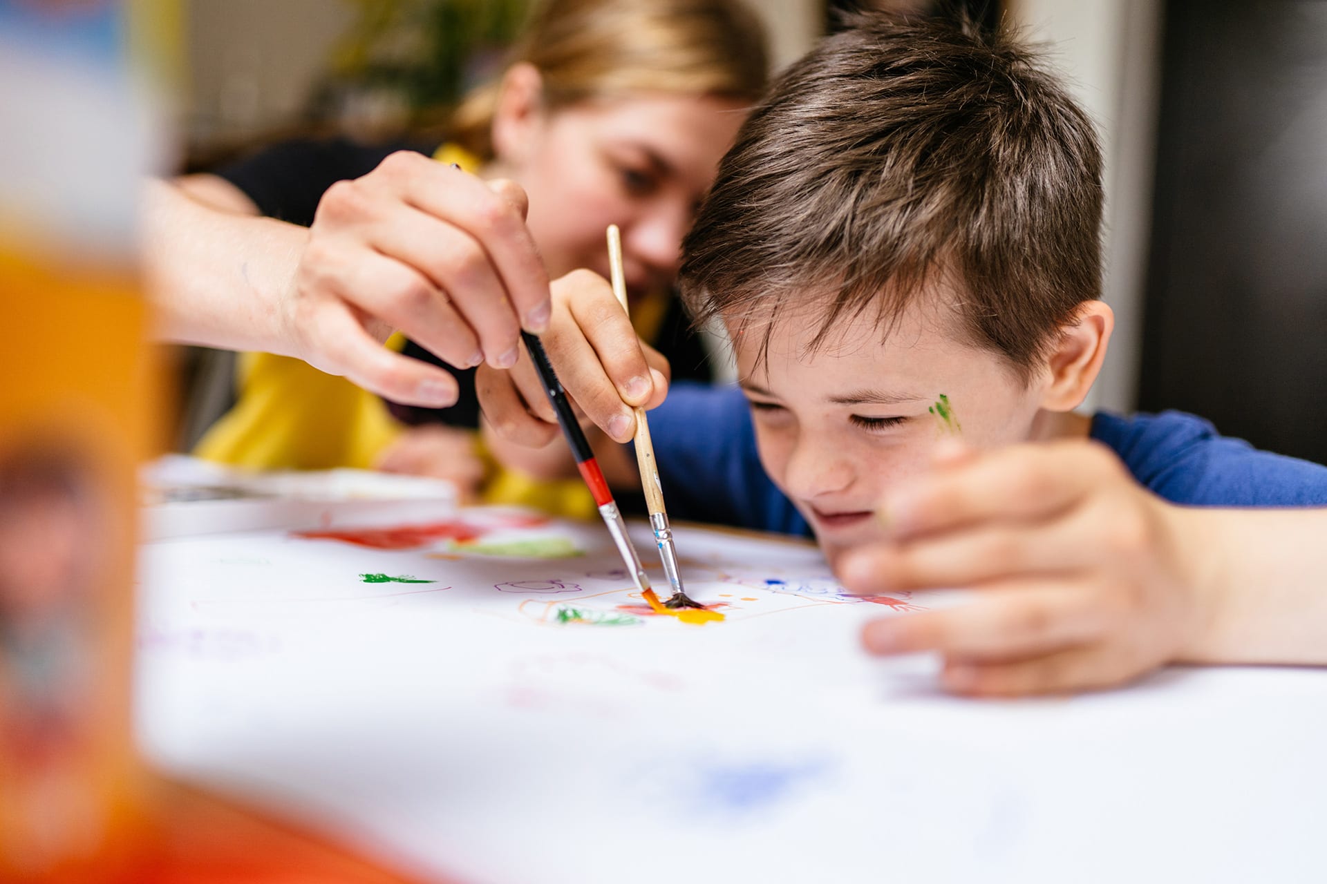 Integrativer Kindergarten | Erzieherin malt mit Pinsel und Hilfestellung mit einem Jungen