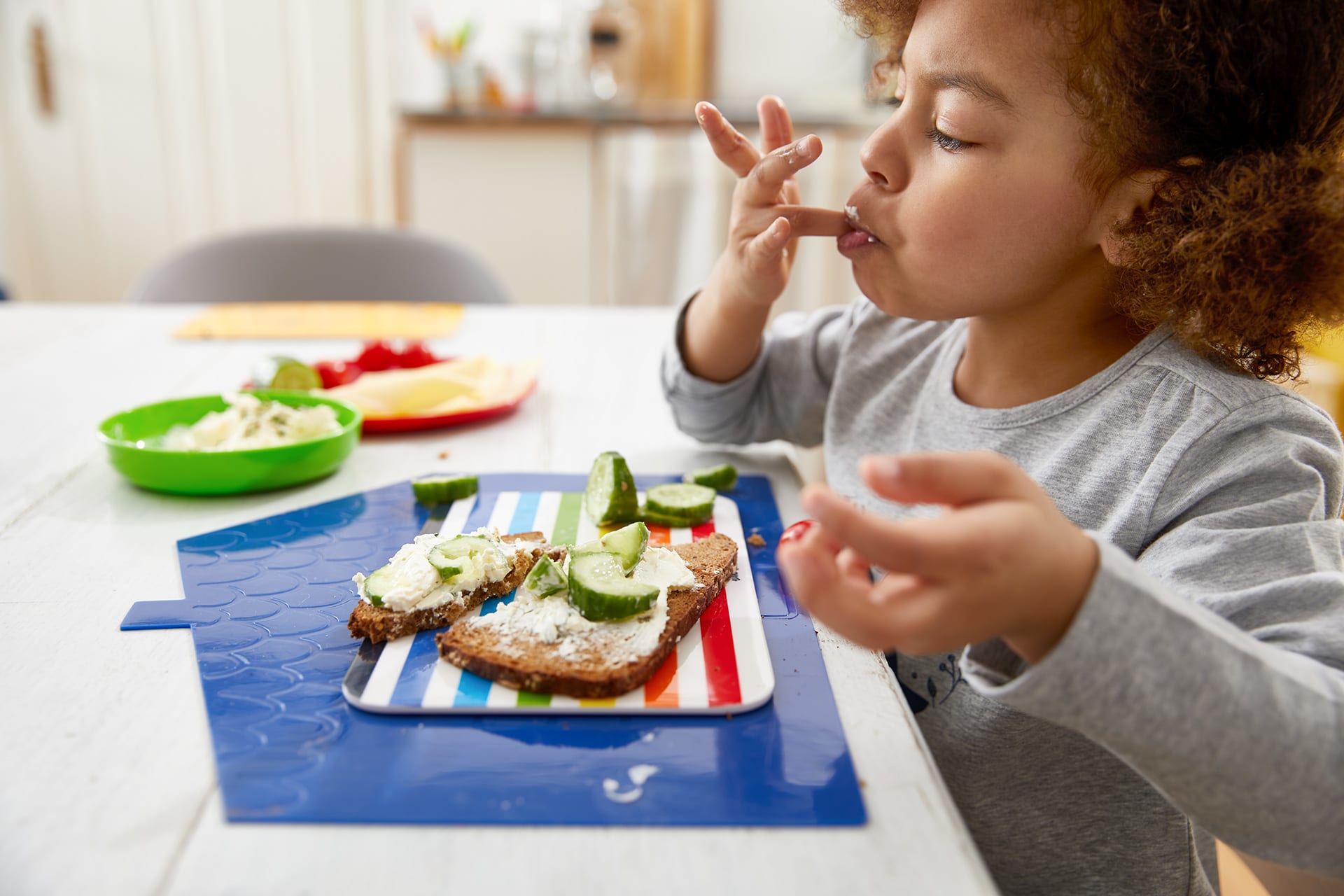 Gesundes Essverhalten | Mädchen sitzt am Tisch und isst mit Finger