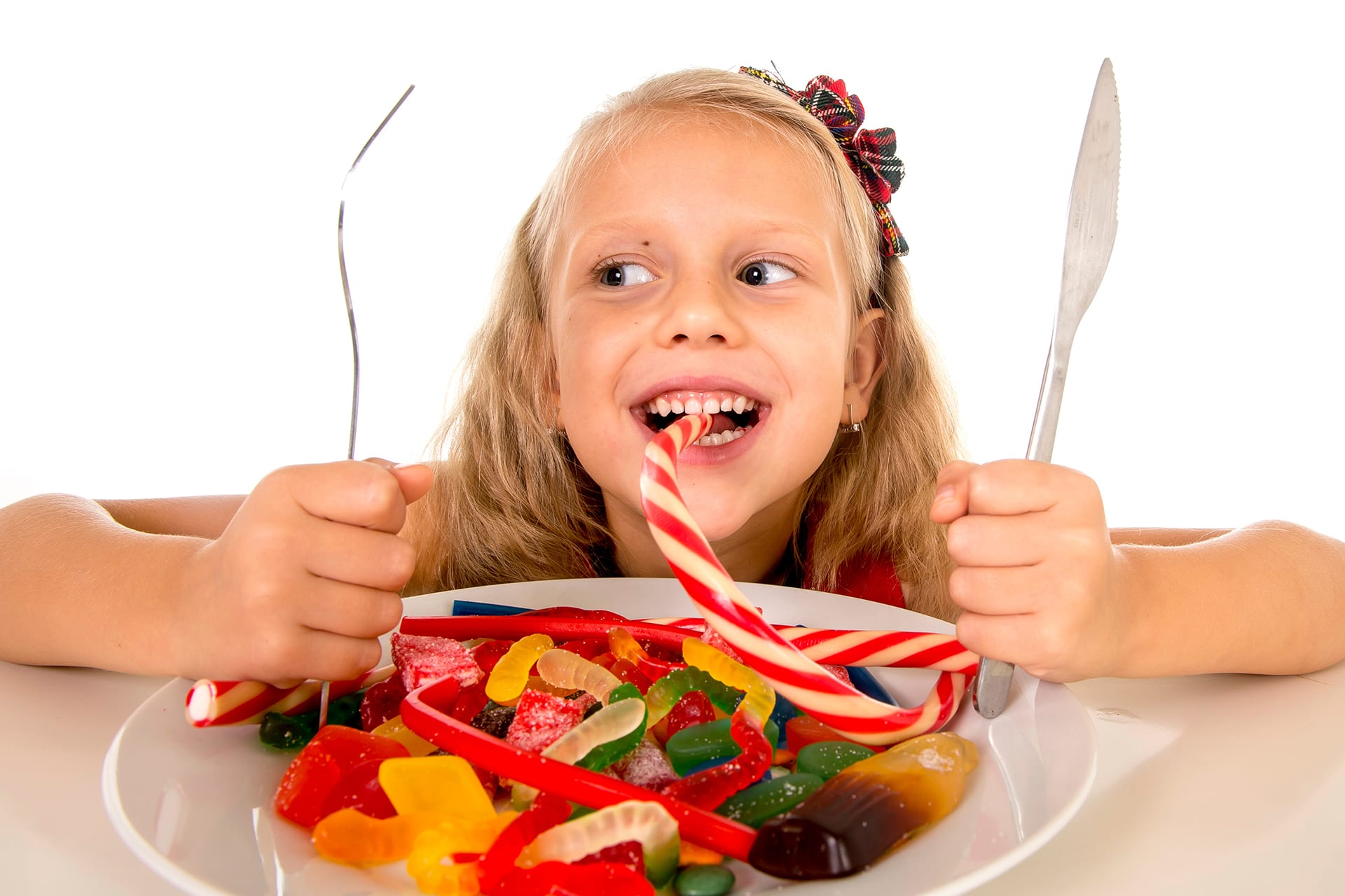 Kinder - Süßigkeiten | Grinsendes Mädchen mit Besteck in den Händen und einem Teller Nascherei