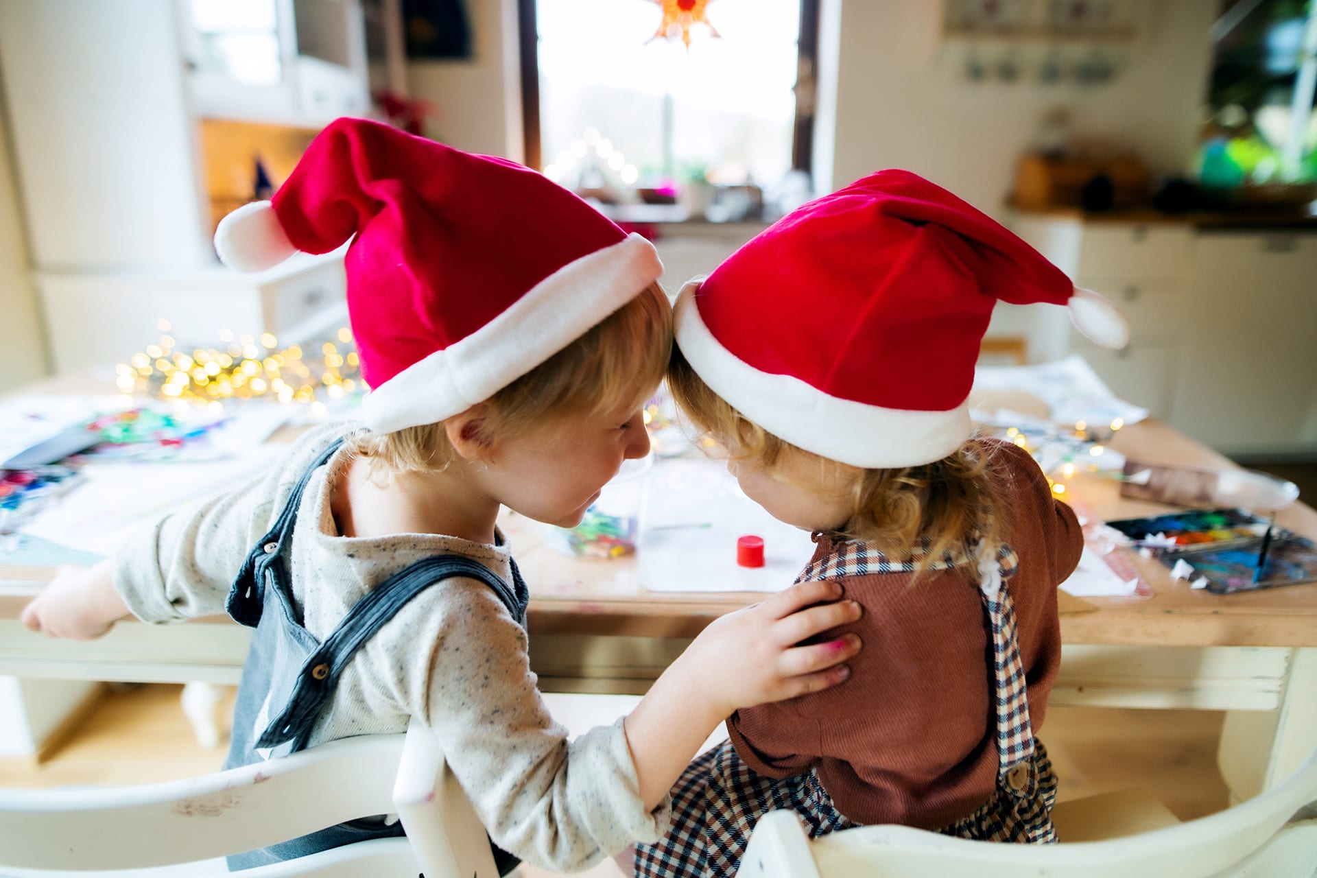 Weihnachts-Wunschzettel | Zwei Kinder mit roten Weihnachtsmützen sitzen am Tisch und basteln