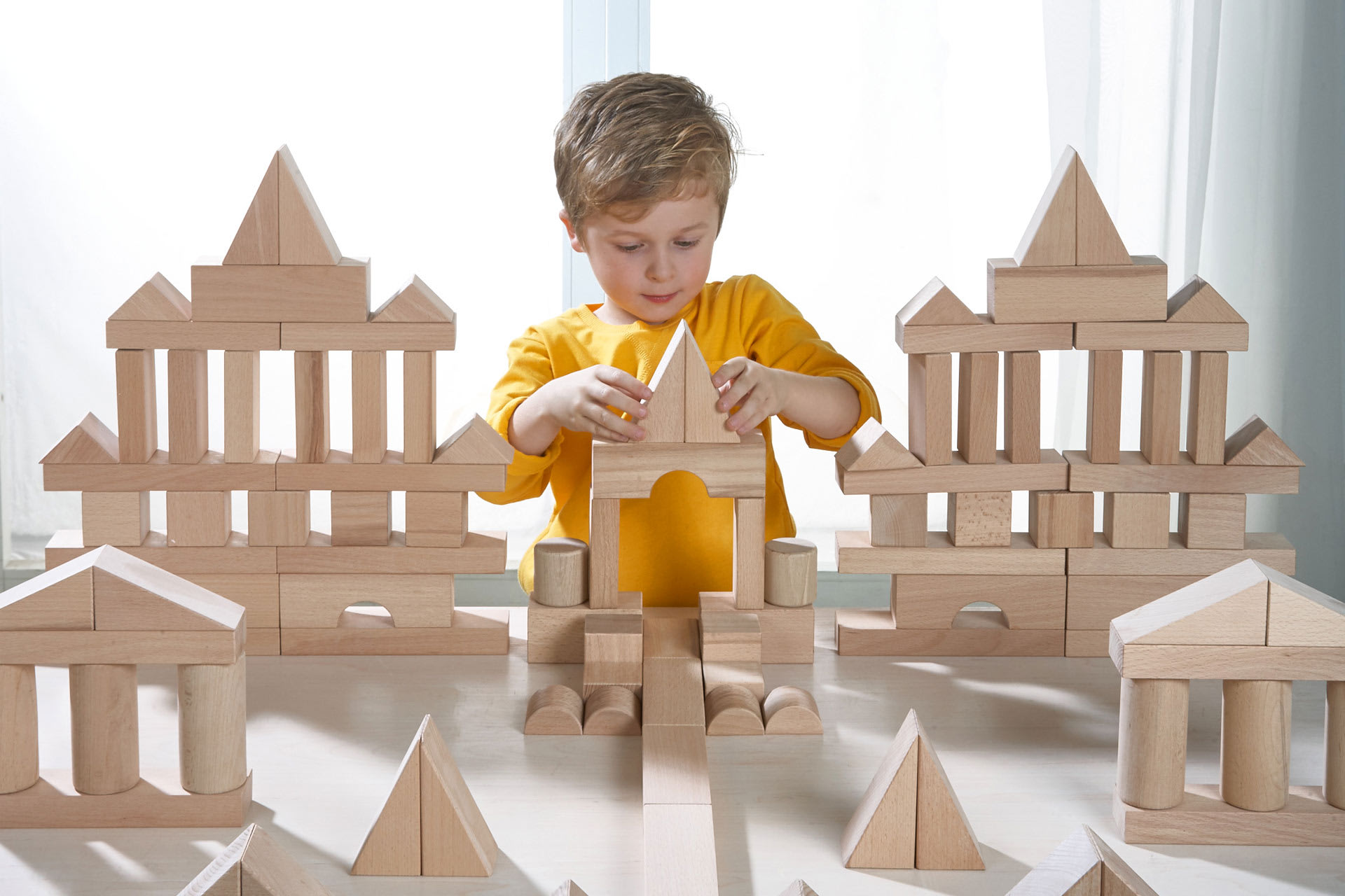 Fröbel - Bauen & Spielen | Junge im gelben Langarmshirt baut einen Turm 