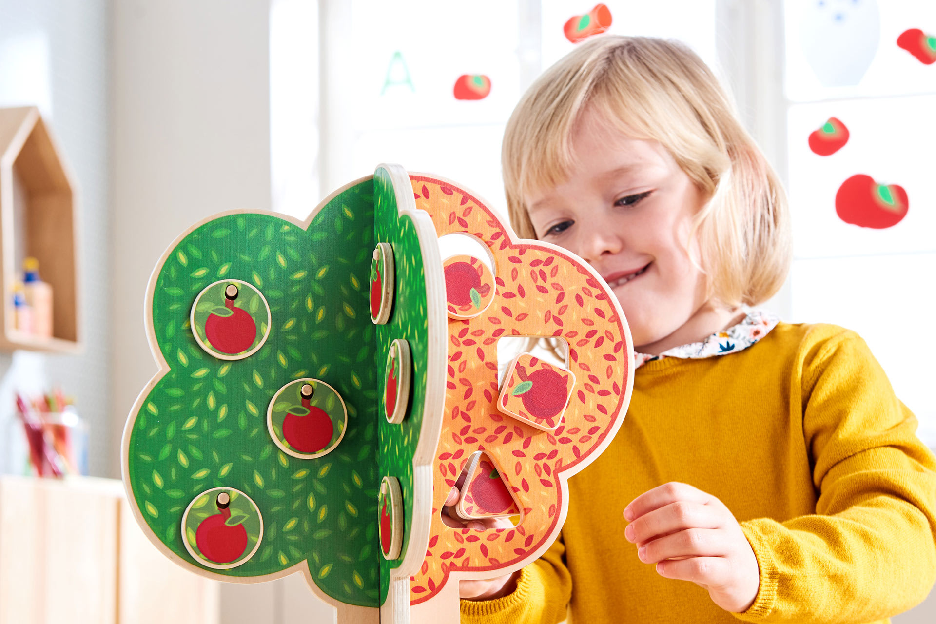 Fröbels Konzept zur Frühen Bildung | blondes Mädchen mit gelben Pulli spielt mit dem Jahreszeitenbaum