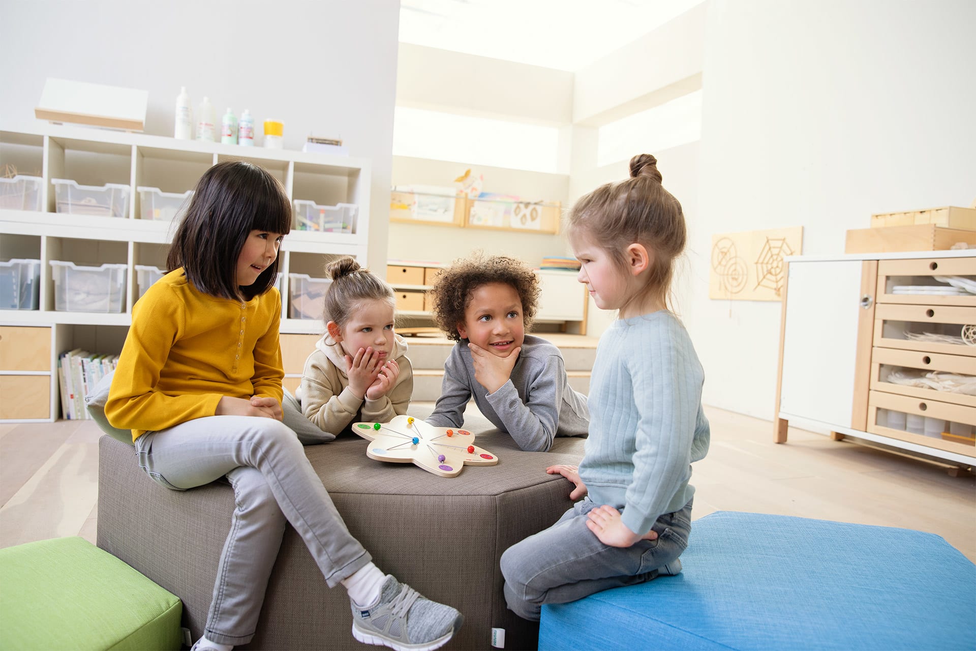 Emotionen | 2 | Image | Emotionsstern | Kinder sitzen zusammen um und auf einem grauen Sitzhocker und spielen mit Emotionsstern