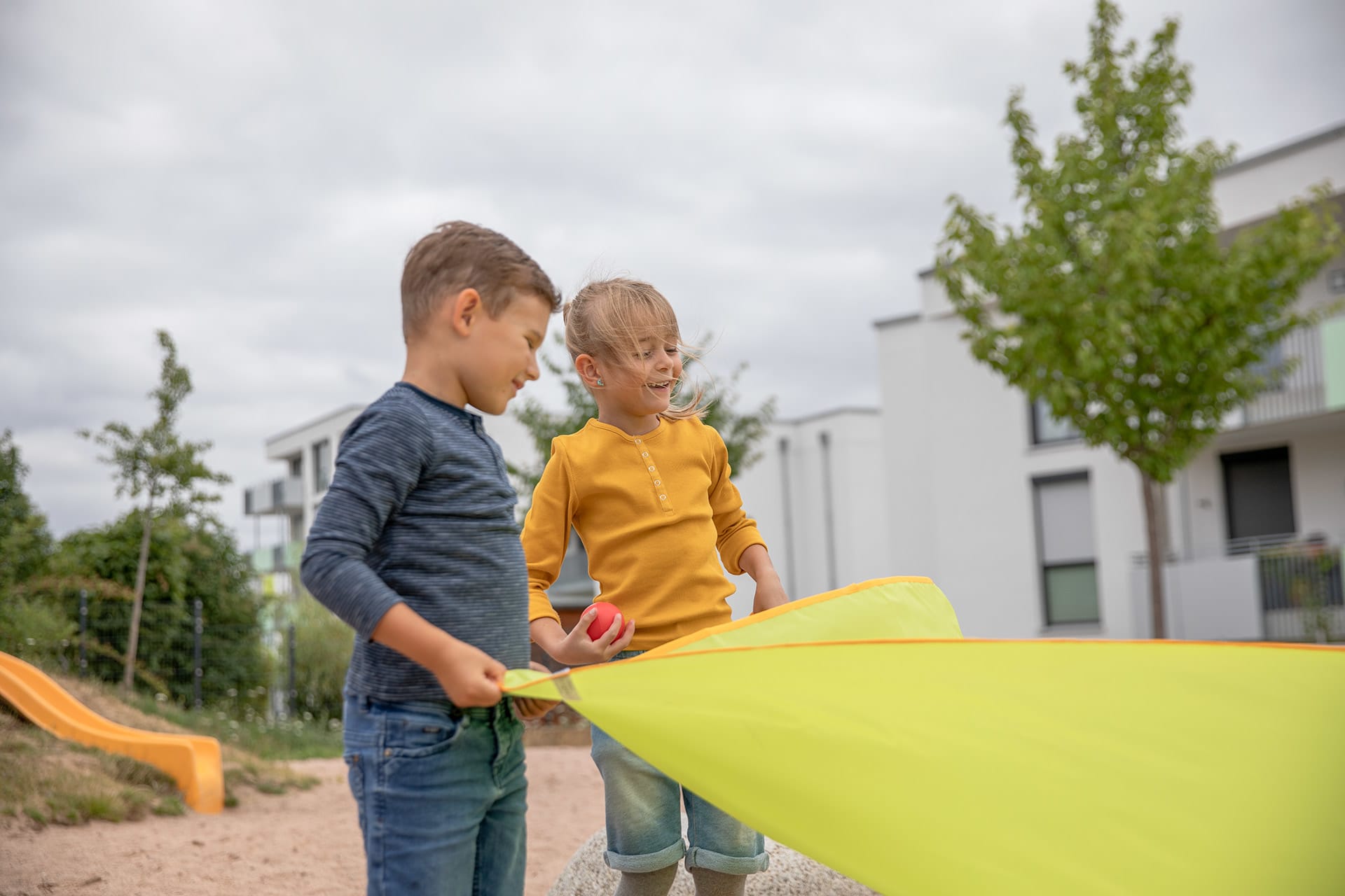 Teamfähigkeit | Image | Junge und Mädchen mit gelben Langarmshirt halten gelbes Schwungtuch fest 