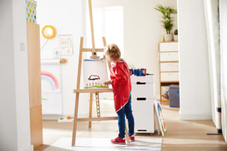 Basteln mit Kindern | Mädchen mit rotem Malkittel, malt ein Bild mit Blumen, an Staffelei