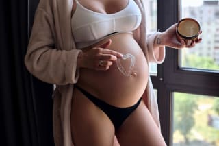 Schwangerschaft 36 SSW | Schwangere Frau sitzt auf grauem Sofa im Schneidersitz