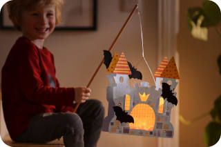 Laternen basteln mit Kindern | Kind hält Laterne in Burgform mit Fledermäusen
