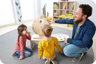 Englisch im Kindergarten | Mann spielt mit Kindern am Holzrad