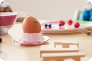 Osterrezepte für Kinder | Braunes Ei mit aufgemaltem Gesicht, in einem Eierbecher, steht auf einem Tisch