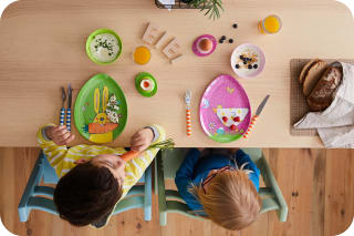 Osterrezepte für Kinder |  zwei Kinder sitzen am Tisch, vor Tellern in Ei-Form mit Ostermotiven