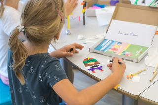 Digitalwerkstatt | Mädchen mit blonden Haaren von hinten fotografiert sitzt am Tisch und spielt mit Digitalwerkstatt Box