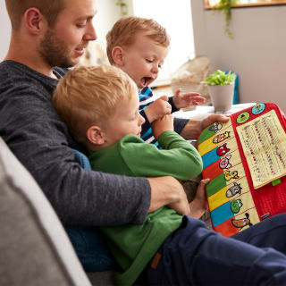 Musik entdecken mit Kinderliedern von HABA | Vater sitzt mit 2 Kindern auf Sofa und spielt mit Stoffklavier