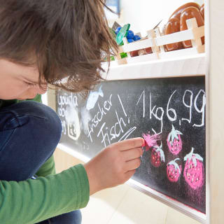 Kinderküche & Kaufladen | Kind schreibt mit Kreide was an die Tafel vom Einkaufsladen
