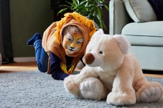Faschingsspiele | Junge als Löwe verkleidet krabbelt auf Teppich. Teddy sitzt im Bild Vordergrund