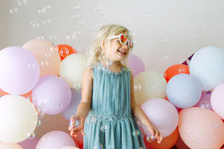 Faschingsspiele Kinder |Mädchen mit Sonnenbrille und Kleid tanzt mit vielen Luftballon und Seifenblasen 