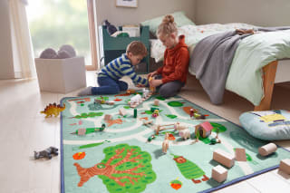 Kinderzimmer einrichten | Junge und Mädchen sitzen im Kinderzimmer auf Boden mit Spielteppich und Spielfiguren