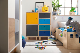 Kinderzimmer einrichten | Junge schmeißt sich in das Bett, Lego Steine liegen auf einem Teppich vor dem Bett