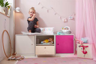 Kinderzimmer einrichten | Mädchen sitzt auf Regalsystem mit weißer und pinker Schranktür