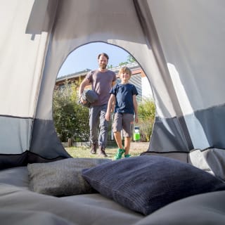 Langeweile in den Ferien | Papa und Sohn stehen vor Zelt mit Schlafsack und Nachtlicht