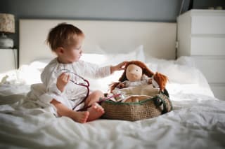 Rollenspiele | Kleinkind hört mit Stethoskop zu einer Puppe Spielzeug im Bett im Schlafzimmer