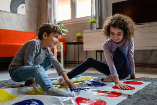 Kinderspiele selber machen | Junge und Mädchen sitzen auf Plane mit farbigen Fußabdrücken