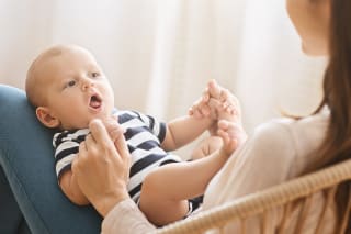 Sprechen lernen | Baby liegt auf Mamas Oberschenkel und hält ihre Hände und spricht mit ihr
