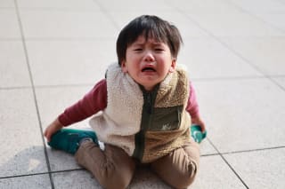 Trotzphase bei Kindern |  Kleiner Junge kniet am Boden, hält die Füße mit Händen fest und weint