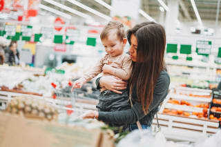 Einkaufen mit Baby | Mutter hebt Kind hoch und zeigt Obst-Theke im Supermarkt