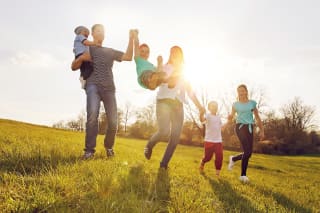 Sport mit Kindern | Eltern springen mit ihren Kindern an der Hand über eine Wiese.