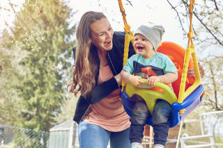 Sport mit Kindern | Baby sitzt draußen in der Schaukel, Mutter schubst an