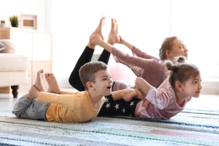 Sport mit Kindern | Mutter macht mit ihren Kindern Yoga auf dem Teppich im Wohnzimmer