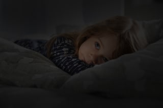 Albträume bei Kindern | Mädchen liegt im Bett, hat Augen offen 