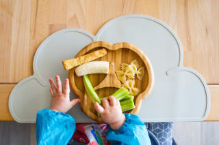 Snacks für Babys & Kleinkinder | Kinderhände greifen auf einem Holzteller nach Gurken, Banane, Nudeln