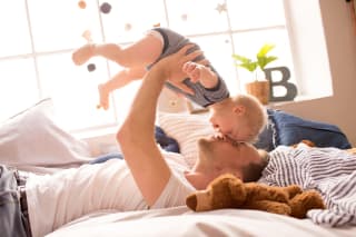 Baby zum Lachen bringen | liegender Vater hält lachendes Baby in die Luft