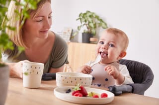 Was ist Baby Led Weaning | Baby isst mit Löffel und die Mutter sitzt daneben
