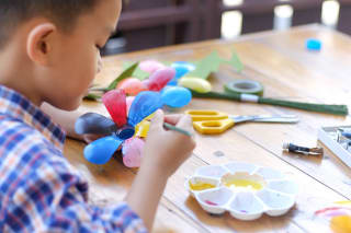 Blumen basteln mit Kindern | Junge bemalt eine Blume aus Plastikflaschen mit einem Pinsel