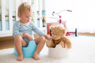 Windelfreie Erziehung | Klein Kind sitzt mit seinem Teddy auf dem Töpfchen